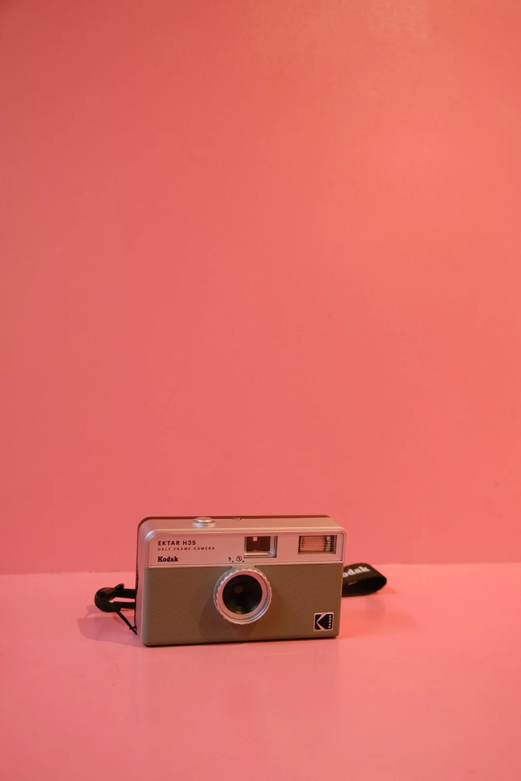 A compact film camera against a coral-pink backdrop.
